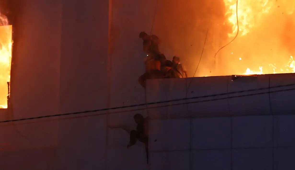 Orang-orang berusaha menyelamatkan diri di birai di sisi kasino hotel Grand Diamond City yang terbakar di Poipet pada 29 Desember 2022. Sebanyak 10 orang tewas dalam kebakaran di kasino-hotel Kamboja di perbatasan Thailand , dengan foto-foto yang menunjukkan kelompok-kelompok berkerumun mati-matian di tepian saat api yang ganas mengelilingi mereka. (AFP/STR)