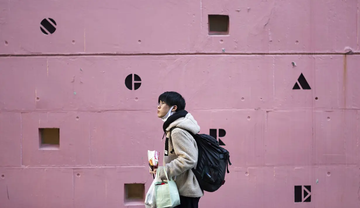 Seorang pria yang meletakkan masker wajah di bawah dagunya sambil makan makanan ringan berjalan melewati sekolah bahasa asing di Tokyo, Jepang,  Kamis (4 /2/2021). Tokyo mengonfirmasi lebih dari 730 kasus baru COVID-19 pada 4 Februari 2021. (AP Photo/Hiro Komae)