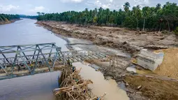 Struktur jembatan baja tersebut ditargetkan menjadi penghubung sementara agar mobilitas masyarakat dan distribusi logistik ke wilayah terdampak dapat kembali berjalan. Tampak foto udara menunjukkan warga memanjat puing-puing untuk menyeberangi sungai di jembatan yang baru dibangun yang menghubungkan Aceh dan Provinsi Sumatera Utara setelah hancur akibat banjir bandang di Sungai Peusangan di Distrik Bireuen, Provinsi Aceh, pada Selasa 9 Desember 2025. (CHAIDEER MAHYUDDIN/AFP)