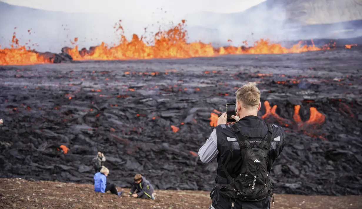 Orang-orang melihat aktivitas di gunung berapi Fagradalsfjall di Islandia pada Rabu (3/8/2022), yang terletak 32 kilometer (20 mil) barat daya ibu kota Reykjavik dan dekat dengan Bandara Internasional Keflavik. Video menunjukkan gunung berapi itu memuntahkan magma dari celah sempit sekitar 100 hingga 200 meter di atas bidang lava dari letusan tahun lalu. (AP Photo/Marco Di Marco)