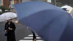 Seorang wanita menggunakan payung berjalan saat hujan turun di Tokyo, Jepang (8/8). Topan kuat sedang mengarah ke Jepang pada 8 Agustus, mendorong badan cuaca untuk memperingatkan akan terjadi hujan lebat dan angin kencang. (AFP Photo/Behrouz)