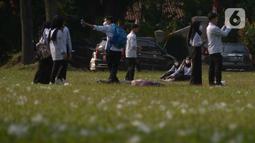 Mahasiswa berfoto di rumput yang bercampur dengan kapas di halaman Institut Pertanian Bogor, Kota Bogor, Jawa Barat, Kamis (25/8/2022). Kapas yang berasal dari pohon kapuk randu yang sedang berguguran itu menjadi daya tarik bagi warga untuk berswafoto. (Liputan6.com/Angga Yuniar)