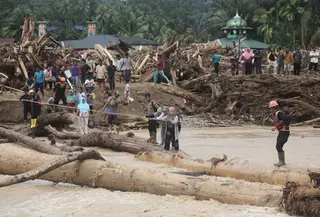Warga yang menjadi korban banjir bandang di Batang Toru, Tapanuli Selatan, Sumatra Utara menggunakan kayu gelondongan untuk menyeberangi sungai, Selasa 2 Desember 2025. Warga Batang Toru, Tapanuli Selatan, terpaksa menggunakan jembatan darurat yang terbuat dari gelondongan kayu untuk menyeberangi sungai setelah jembatan utama rusak akibat terjangan banjir bandang baru-baru ini. (AP Photo/Binsar Bakkara)