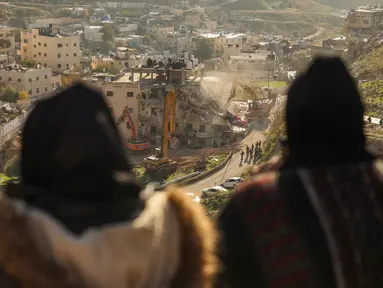 Para perempuan Palestina menyaksikan pasukan Israel yang menggunakan ekskavator merobohkan sebuah bangunan yang dibangun tanpa izin di lingkungan Wadi Qaddum, Yerusalem timur, pada Senin 22 Desember 2025. Ratusan warga Palestina terusir saat buldoser-buldoser Israel meratakan sebuah bangunan tempat tinggal empat lantai di wilayah Yerusalem Timur. (Ahmad GHARABLI/AFP)