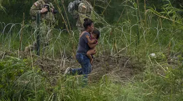 Petugas Garda Nasional Texas berdiri di sepanjang bentangan kawat berduri saat migran perempuan yang membawa seorang anak mencoba menyeberang ke AS, di tepi Rio Grande, seperti yang terlihat dari Matamoros, Meksiko, Kamis (11/5/2023). (AP Photo/Fernando Llano)