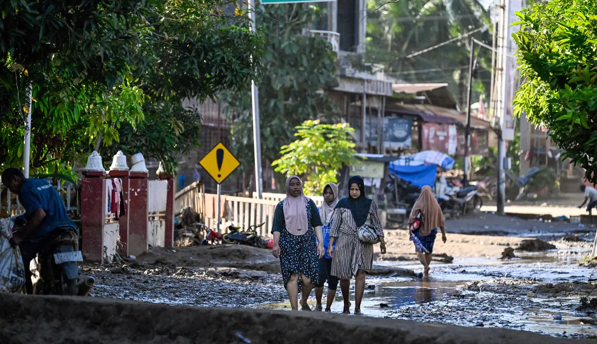 Sebelumnya, curah hujan ekstrem sejak Kamis (27/11) malam hingga Jumat (28/11/2025) dini hari memicu bencana hidrometeorologi di 14 kecamatan di Pidie Jaya. Tampak dalam foto, orang-orang berjalan di jalan yang tertutup lumpur setelah banjir bandang di Meureudu, Kabupaten Pidie Jaya, Provinsi Aceh, pada 29 November 2025. (CHAIDEER MAHYUDDIN/AFP)