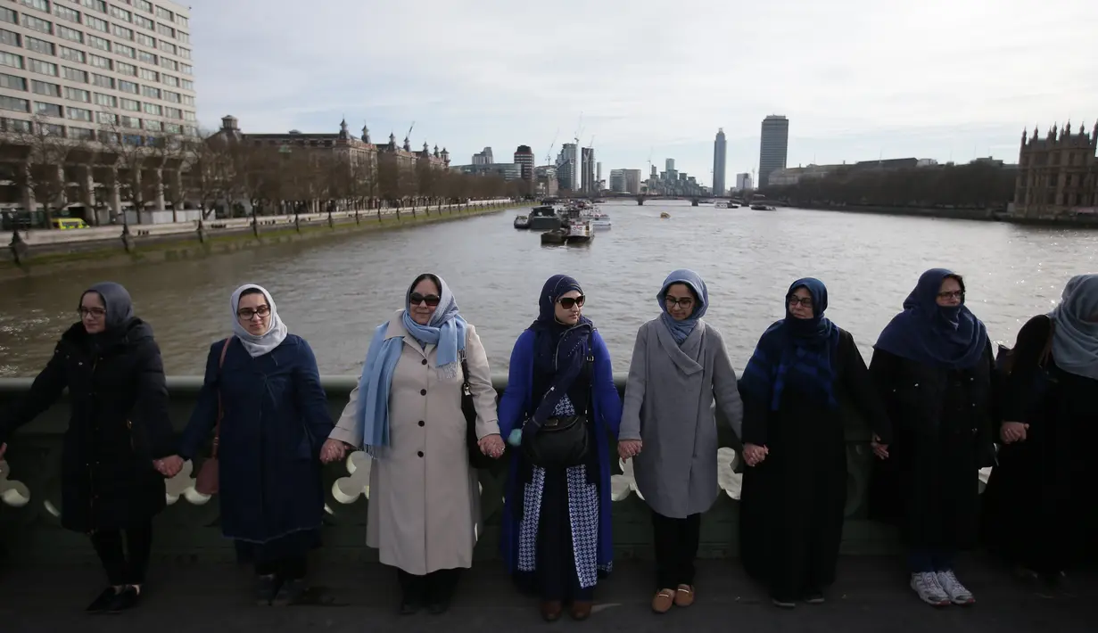 Barisan perempuan mengenakan warna biru bergandengan tangan di Jembatan Westminster, London, Minggu (26/3). Mereka mengenakan biru sebagai simbol harapan dan  bergenggaman tangan sepanjang jembatan tempat teror London terjadi. (Daniel LEAL-OLIVAS/AFP)