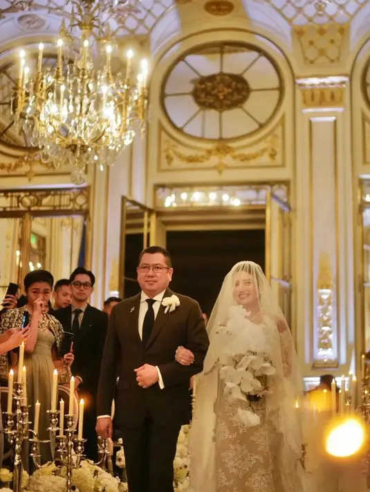 Mempelai perempuan tampil angun dengan gaun putih lengkap dengan veil  panjang. Berjalan digandeng ayah tercinta, Hary Tanoesoedijo. Senyum manis Valencia di hari pemberkatan nikah.  [Instagram/diah_kss]