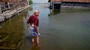 Sukarman berjalan di jalur banjir di luar rumahnya di Timbulsloko, Jawa Tengah, Indonesia, 30 Juli 2022. Sukarman berpikir anak muda, seperti cucunya Dwi Ulfani, harus mencoba keluar dari desa jika mereka bisa. Tapi dia pasrah dengan kenyataan bahwa tanpa uang atau rumah keluarga lainnya, dia kemungkinan akan menghabiskan sisa hidupnya tinggal di rumah yang semakin banjir. (AP Photo/Dita Alangkara)