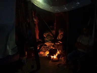Warga Palestina yang mengungsi akibat pengeboman Israel di Jalur Gaza duduk di dekat api di kamp tenda yang disediakan oleh UNDP di Khan Younis, Rabu, 1 November 2023. (AP Photo/Fatima Shbair)