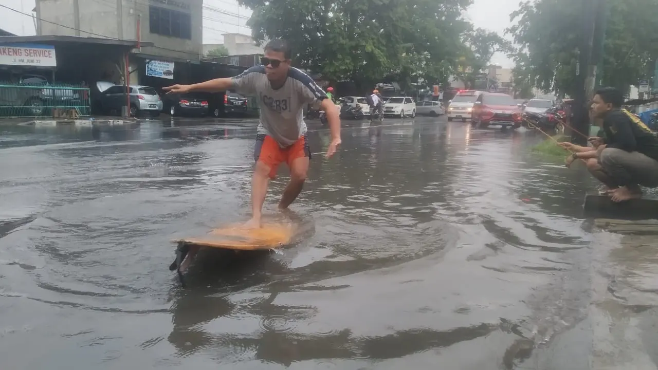 Warga berselancar saat banjir di Medan.