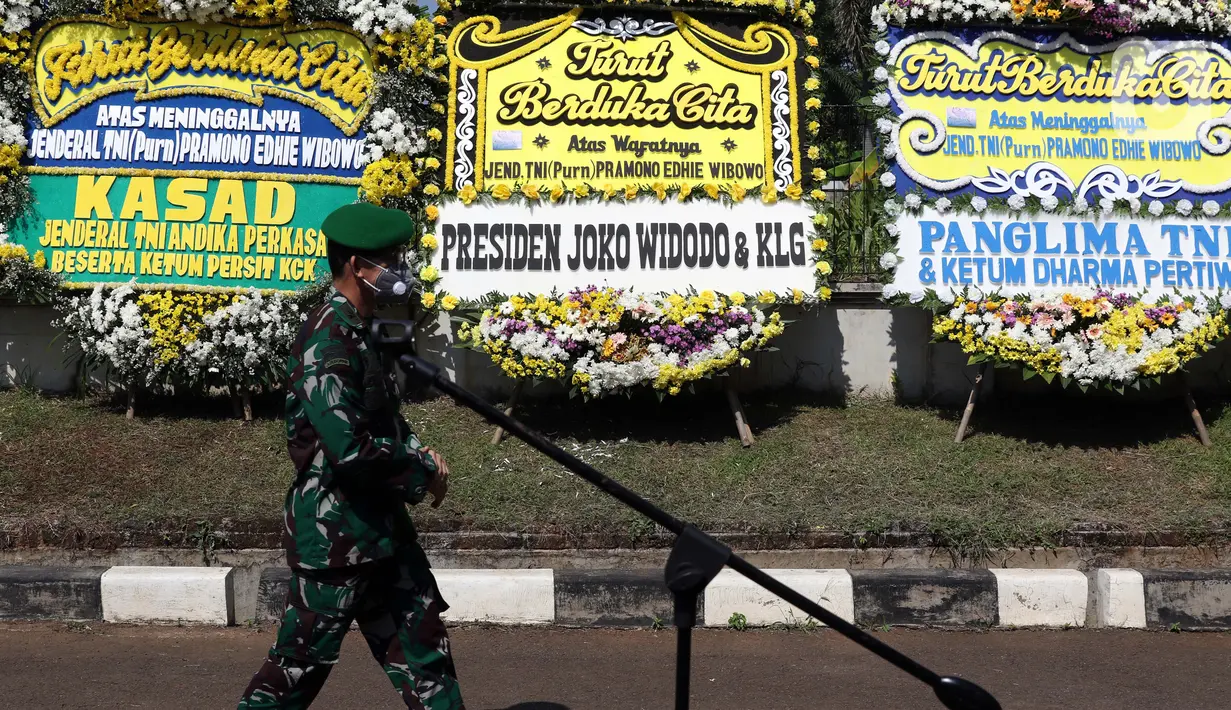 Prajurit TNI melintas di depan karangan bunga tanda duka cita atas meninggalnya mantan KSAD Jenderal TNI (Purn) Pramono Edhie Wibowo di kawasan Puri Cikeas, Kab Bogor, Jabar, Minggu (14/6/2020). Pramono Edhie Wibowo wafat di usia 65 tahun akibat serangan jantung. (Liputan6.com/Helmi Fithriansyah)