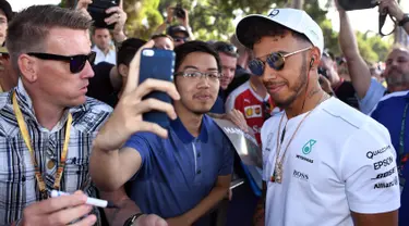 Pembalap Mercedes, Lewis Hamilton melakukan selfie dengan seorang penggemar menjelang sesi latihan bebas pertama di Grand Prix Australia, Melbourne, Jumat (24/3). (AFP Photo/WILLIAM WEST)