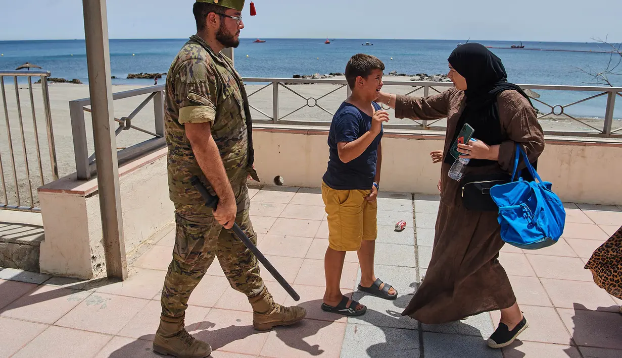 Seorang wanita berbicara dengan seorang migran berusia 12 tahun tanpa pendamping sementara seorang tentara Spanyol mengawal anak tersebut ke perbatasan Spanyol-Maroko dari wilayah kantong Spanyol di Ceuta, Senin, 3 Agustus 2026. (Foto AP/Bernat Armangue)