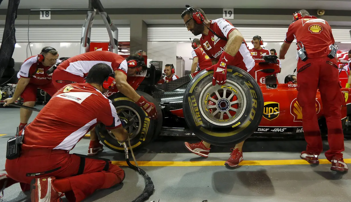 Mekanik Ferrari menganti ban jelang ajang sesi latihan Grand Prix Singapura F1 (18/9/2015). Kabut asap yang menyelimuti sirkuit tak menyurutkan pembalap untuk tetap melakukan pemanasan. (REUTERS/Olivia Harris)