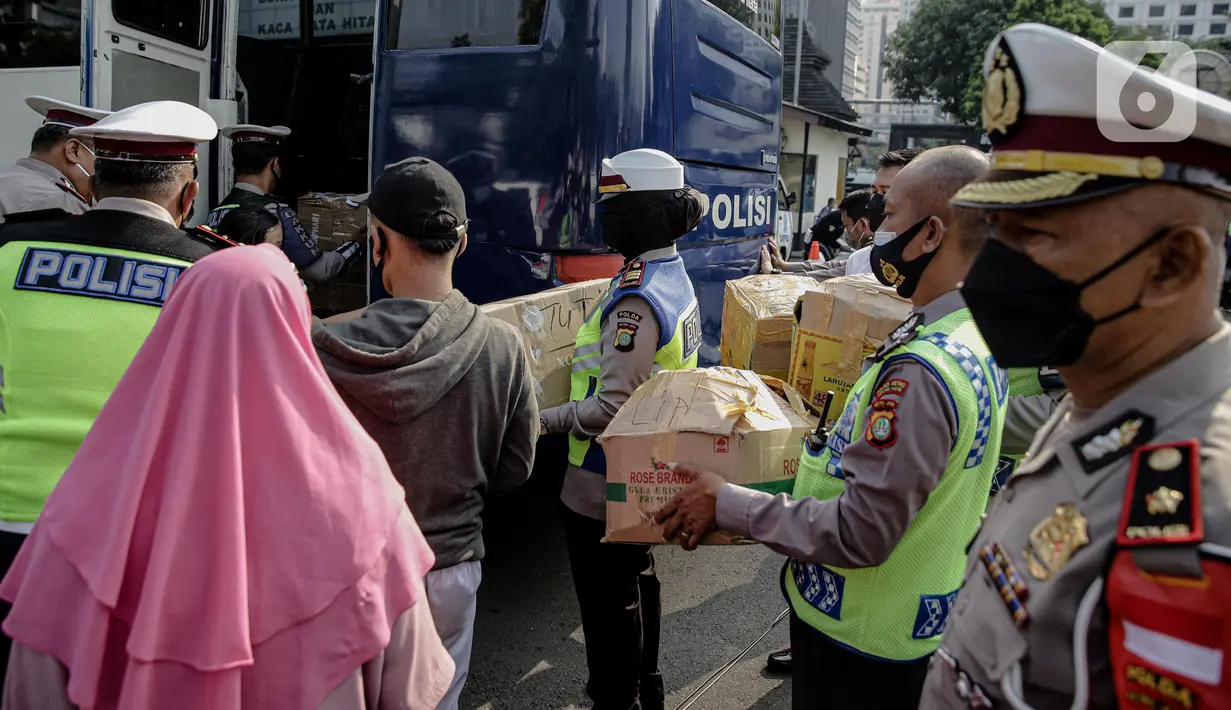 Polisi membantu membawakan barang penumpang yang terjaring razia travel gelap Ditlantas Polda Metro Jaya saat akan dipulangkan ke daerah asalnya, Jakarta, Kamis (29/4/2021). Sebanyak 115 kendaraan travel gelap diamankan. (Liputan6.com/Faizal Fanani)