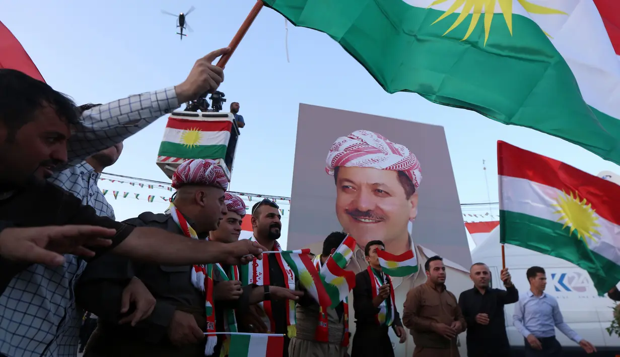Warga Kurdi Irak berkumpul sambil melambai-lambaikan bendera Kurdi di samping poster Pemimpin Kurdi, Massoud Barzani saat melakukan aksi untuk meminta referendum kemerdekaan di Arbil, Irak utara (13/9). (AFP Photo/SAfim Hamed)
