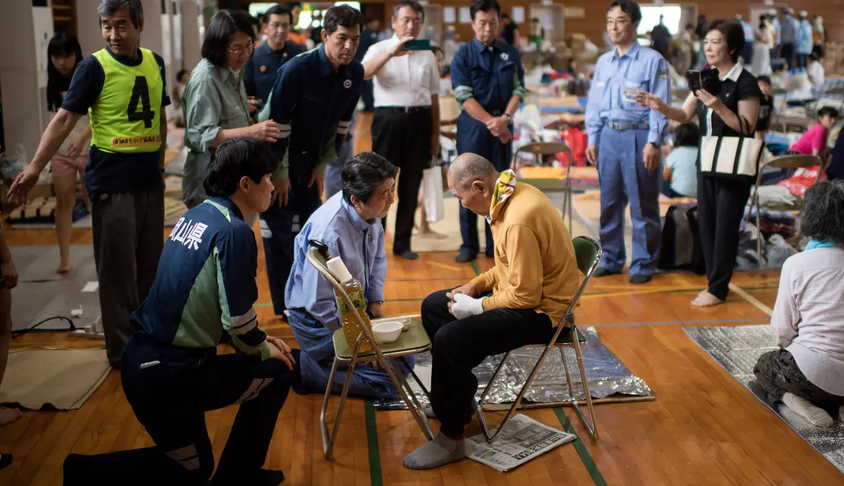 Perdana Menteri Jepang Shinzo Abe mengunjungi pusat evakuasi korban banjir di Mabi, Prefektur Okayama, Rabu (11/7). Regu petugas pemadam kebakaran dari luar prefektur juga dikerahkan untuk melakukan misi pencarian korban. (AFP/Martin BUREAU)