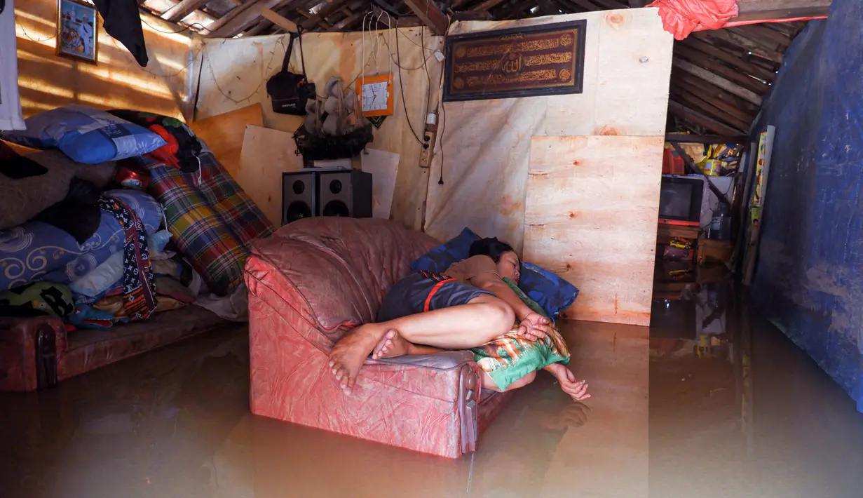 Seorang warga beristirahat di sofa di rumahnya yang terendam banjir di desa Sukajaya di Serang (1/3/2022).  Banjir merendam Kota Serang akibat hujan deras yang turun sejak Senin malam (28/2/2022) hingga hari ini. (AFP/Dziki Oktomauliyadi)