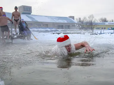 Seorang pria berpakaian seperti Ded Moroz (Santa Claus) berenang di air sedingin es selama hari yang membekukan di kota Omsk di Siberia, Rusia, Sabtu (26/12/2020). Suhu di Omsk turun hingga -32 derajat Celcius atau -25,6 derajat Fahrenheit. (AP Photo/Evgeniy Sofiychuk)