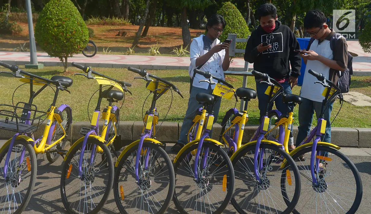 Pengunjung bermain handphone saat akan menggunakan sepeda dari layanan bike sharing di Monas, Jakarta, Jumat (27/7). Layanan bike sharing dapat diakses melalui aplikasi GOWES. (Merdeka.com/Imam Buhori)
