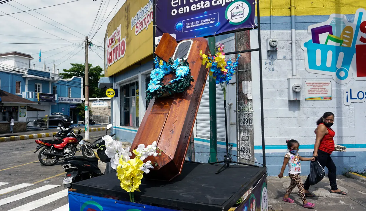 Warga berjalan dekat peti mati dengan tulisan, "Anda memutuskan, di rumah atau di dalam kotak ini", sebagai bagian dari kampanye pemerintah setempat di jalan-jalan kotamadya Escuintla, Guatemala City pada 21 Juli 2020. Kampanye itu sebagai upaya menghentikan penyebaran COVID-19. (Johan ORDONEZ/AFP)