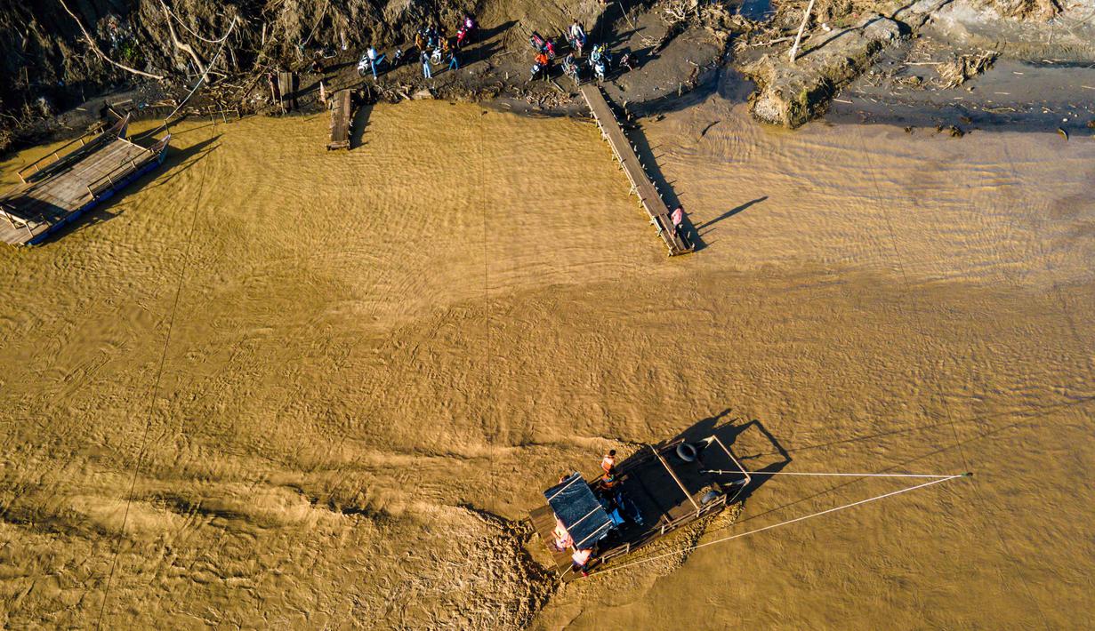 Derasnya air Sungai Peusangan yang menghantam dapat membuat rakit tali berguncang dan rawan kehilangan keseimbangan. Tampak dalam foto, pemandangan udara menunjukkan orang-orang menyeberangi sungai Peusangan menggunakan rakit setelah banjir bandang yang menghancurkan desa-desa di sekitarnya di Kabupaten Bireuen, provinsi Aceh, pada Senin 5 Januari 2026. (CHAIDEER MAHYUDDIN/AFP)