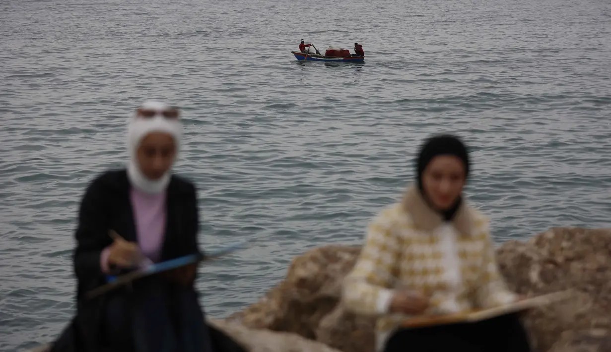 Lokakarya ini merupakan sebuah inisiatif terapi seni pemulihan (healing art) yang ditujukan bagi anak muda dan perempuan di Jalur Gaza. Tampak dalam foto, para perempuan muda melukis berlatar seorang pria yang mengemudikan perahu di pelabuhan Kota Gaza pada Kamis 12 Februari 2026. (Omar AL-QATTAA/AFP)
