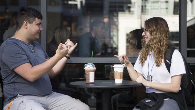 Mahasiswi jurusan penerjemah bahasa isyarat, Nikolas Carapellatti (kiri) berbincang dengan mahasiswi tuna rungu Rebeca Witzofsky di luar kafe Starbucks yang pertama menyediakan layanan bahasa isyarat, di Washington DC, 23/10/2018. (AFP via VOA Indonesia)