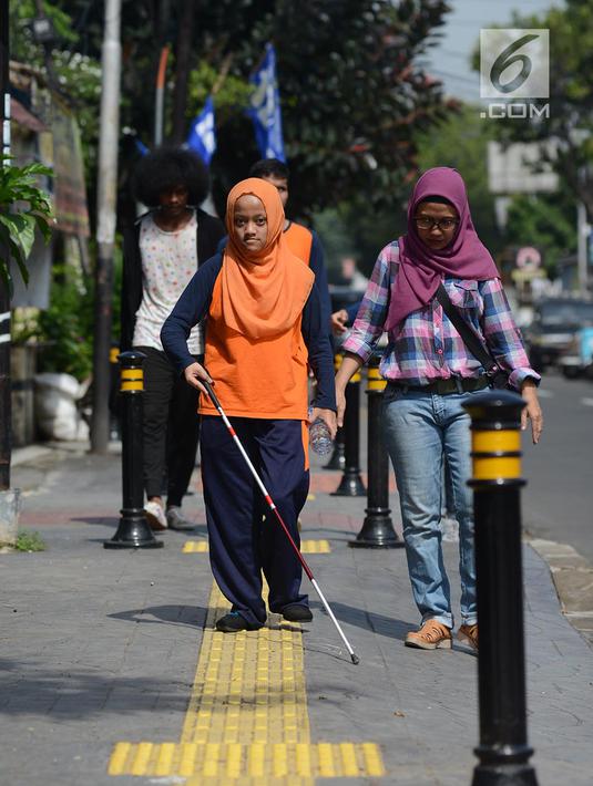 Penyandang disabilitas netra berjalan menyusuri ubin pemandu saat kampanye kegunaan ubin pemandu di trotoar Rawamangun, Jakarta, Selasa (2/4/2019). Kegiatan tersebut untuk memberikan pemahaman kepada masyarakat luas agar tidak terjadi penyalahgunaan di area ubin pemandu. (merdeka.com/Imam Buhori)