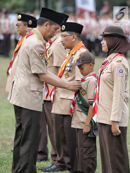 Presiden Joko Widodo memberi tanda kehormatan kepada seorang anak saat perayaan hari jadi Pramuka yang ke-57 di Lapangan Gajah Mada, Wiladatika, Cibubur, Jakarta, Selasa (14/8). (Liputan6.com/Faizal Fanani)
