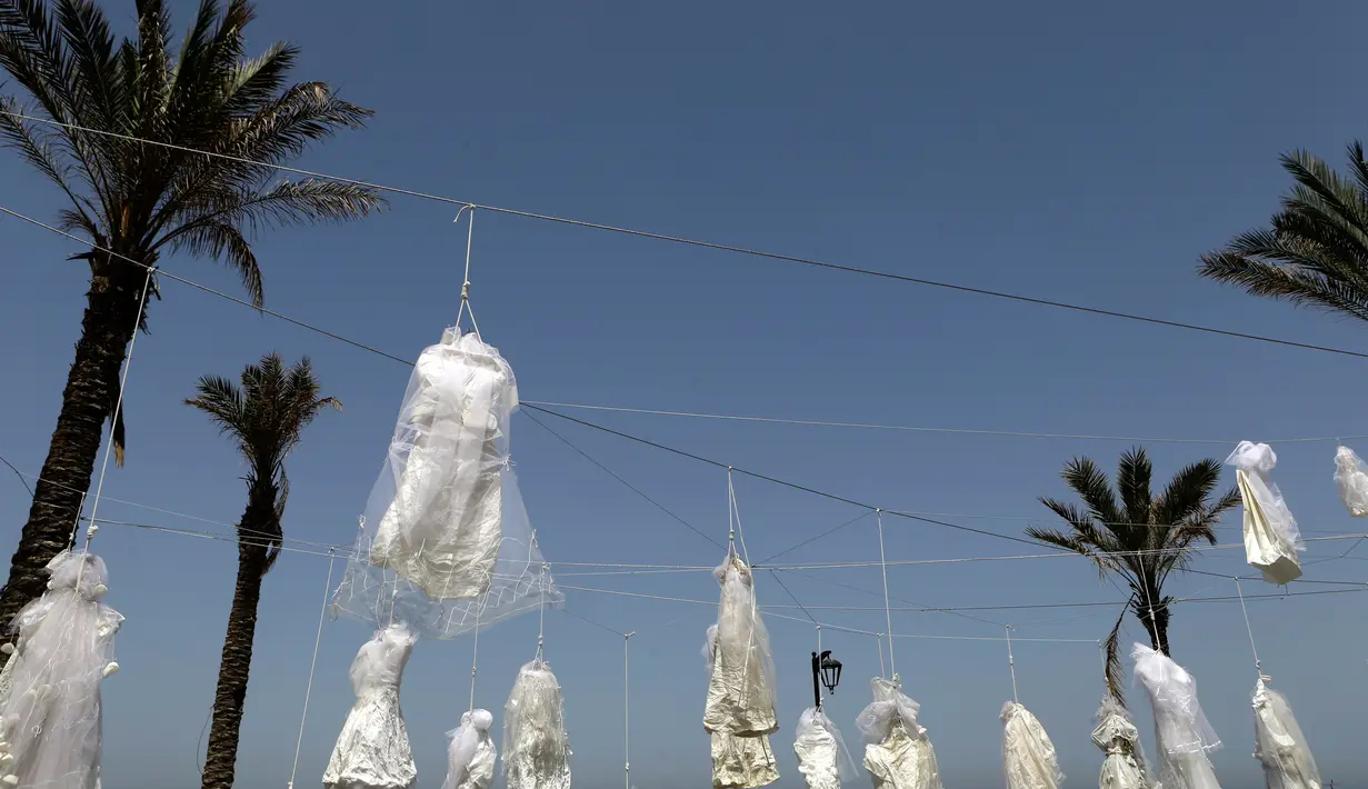 Sejumlah gaun pengantin digantung di antara pohon palem di tepi pantai Beirut, Sabtu (22/4). Sekitar 30 gaun pengantin menggambarkan kondisi mencekam, lusuh dan berwarna pudar sebagai bentuk protes Undang-Undang Pemerkosaan di Lebanon. (PATRICK BAZ/AFP)