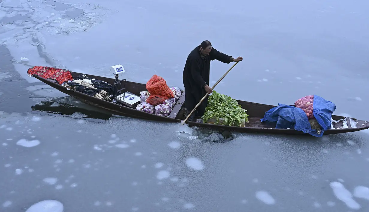 Seorang pria mengendarai sebuah kapal yang penuh dengan sayuran di dekat bagian beku danau Dal setelah hujan salju lebat di Srinagar (16/1/2020). Lapisan tipis es menutupi perairan Danau Dal di Srinagar. (AFP Photo/Tauseef Mustafa)