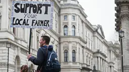 Seorang pria memegang plakat berisi tuntutannya dalam aksi protes oleh petani lokal di Downing Street, pusat kota London, Inggris, Rabu (23/3). (LEON Neal/AFP)