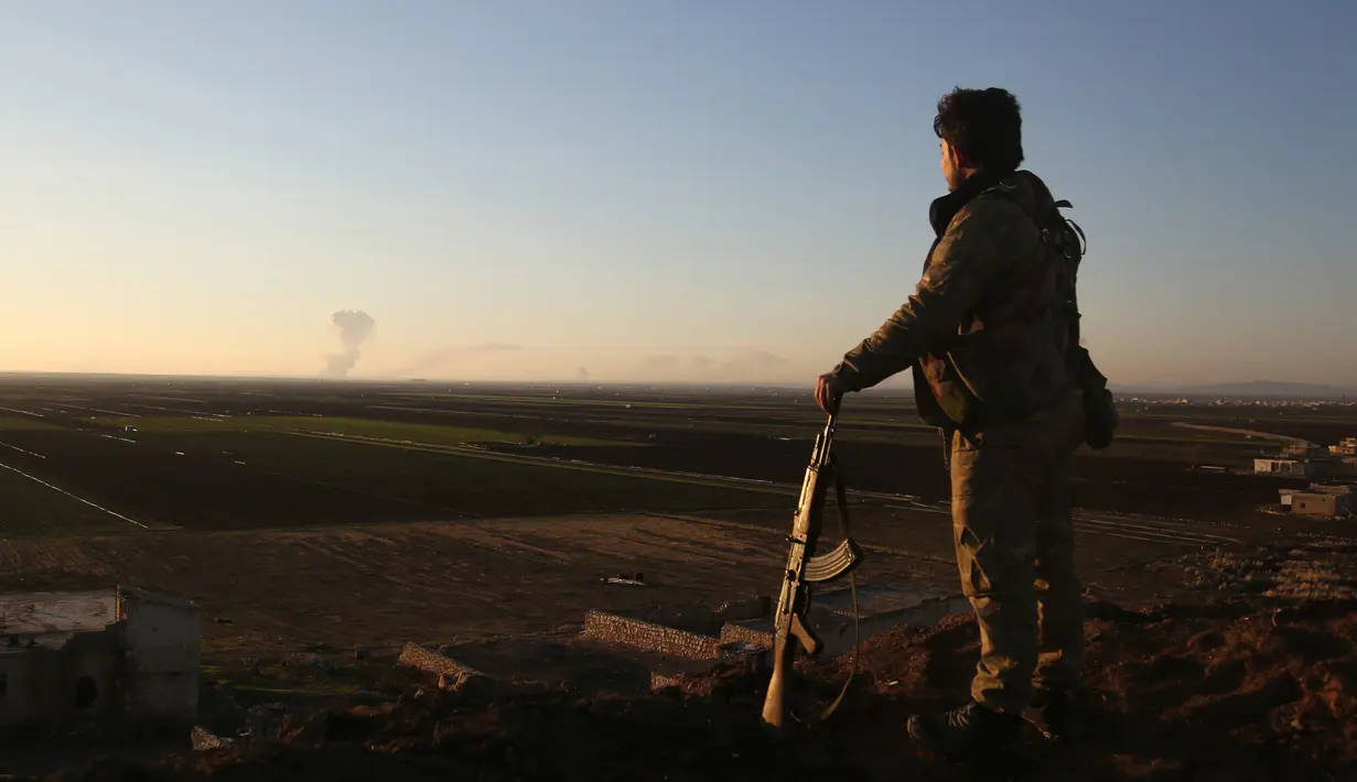 Seorang pejuang Suriah berdiri di daerah Tal Malid, sebelah utara Aleppo, saat dia melihat asap mengepul dari posisi Unit Pertahanan Rakyat Kurdi (YPG) di wilayah Afrin, Suriah, Sabtu (20/1). (AFP FOTO/Nazeer al-Khatib)