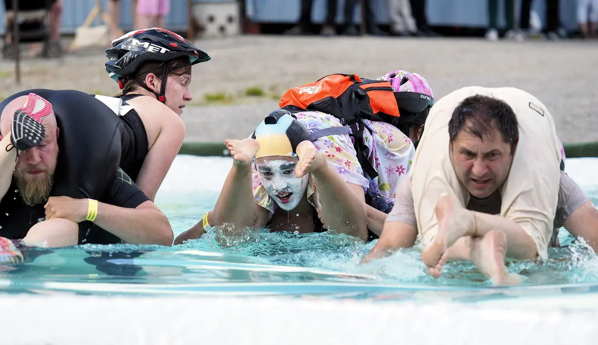 Tiga peserta melintasi kolam sambil menggendong istrinya selama kompetisi Wife Carrying World Championships di Sonkajarvi, Finlandia, 2 Juli 2016. Pemenang kompetisi ini adalah mereka yang tercepat mencapai finish. (Timo Hartikainen/Lehtikuva/AFP)