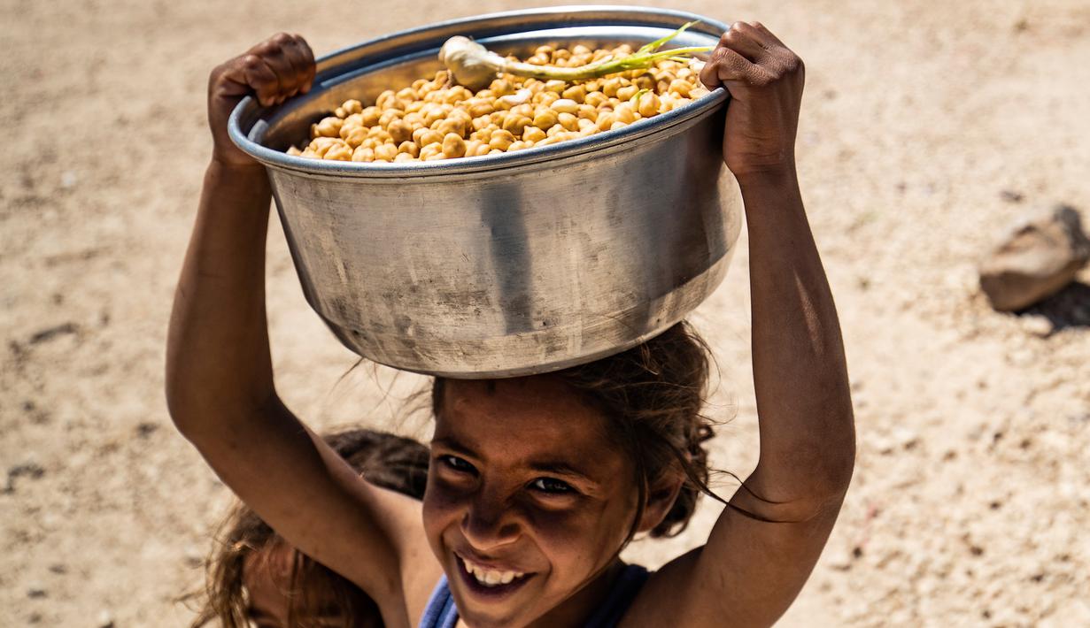 Seorang gadis Suriah yang terlantar membawa sepanci buncis selama bulan suci Ramadan di kamp Washukanni untuk para pengungsi internal di provinsi Hasakeh di timur laut Suriah, (10/5/2020). (AFP/Delil Souleiman)