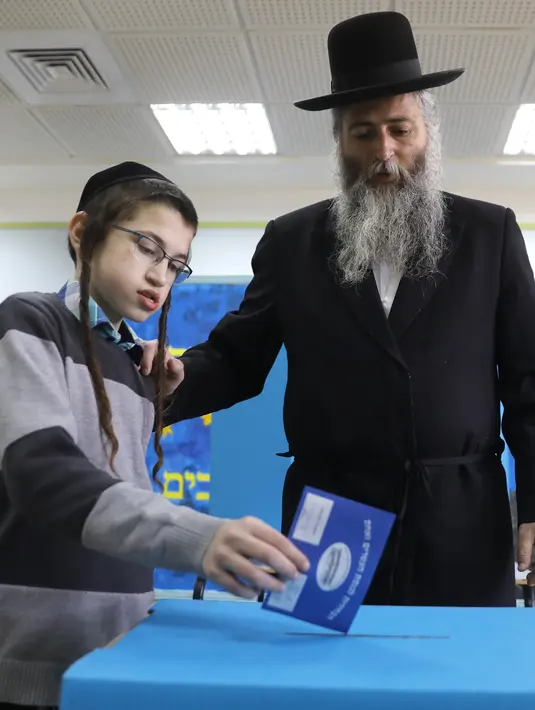 Seorang anak laki-laki memasukan surat suara pria Yahudi ultra-Ortodoks selama pemilihan parlemen Israel di Yerusalem (9/4). Warga Israel hari ini memberikan suara dalam pemilihan tingkat tinggi yang akan memutuskan masa jabatan PM Benjamin Netanyahu. (AFP Photo/Menahem Kahana)