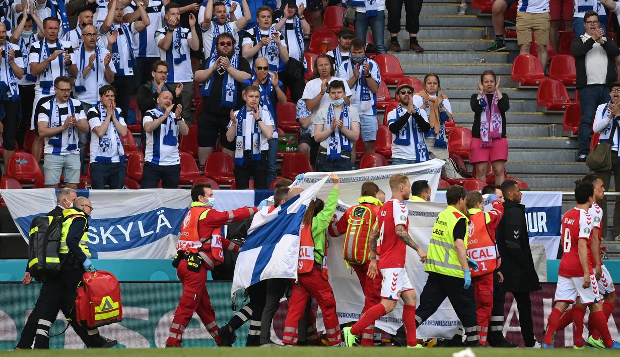 Bendera Finlandia juga menjadi salah satu pahlwan bagi Eriksen. Bendera yang diberikan oleh salah satu suporter Finladia itu berjasa untuk menutupi keadaan Eriksen yang terkulai lemas dari seisi Stadion Parken. (Foto: AFP/Pool/Jonathan Nackstrand)