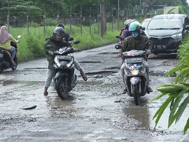 Pengendara motor berusaha menghindari jalan rusak yang menjadi kubangan air di Jalan Raya Gas Alam, Depok, Jawa Barat, Selasa (7/5). Kondisi jalan yang tidak kunjung diperbaiki tersebut menjadi kubangan air setiap hujan serta berbahaya bagi keselamatan pengguna jalan (Liputan6.com/Immanuel Antonius)