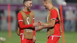 Gelandang Maroko, Hakim Ziyech berbicara reken setimnya Selim Amallah selama sesi latihan di Stadion Al Duhail SC di Doha (16/12/2022). Maroko akan bertanding melawan Kroasia untuk memperebutkan juara 3 Piala Dunia 2022. Keduanya dipertemukan kembali setelah pernah bertanding pada babak penyisihan grup F lalu. (AFP/Karim Jafaar)