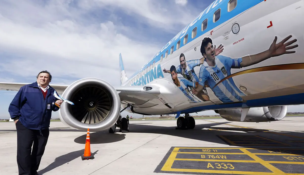 Dengan memegang sebuah replika, salah satu kru Bandara Ezeiza, Buenos Aires berfoto disamping pesawat yang akan digunakan untuk mengangkut Timnmas Argentina menuju Brasil, (3/6/2014). (REUTERS/Marcos Brindicci)