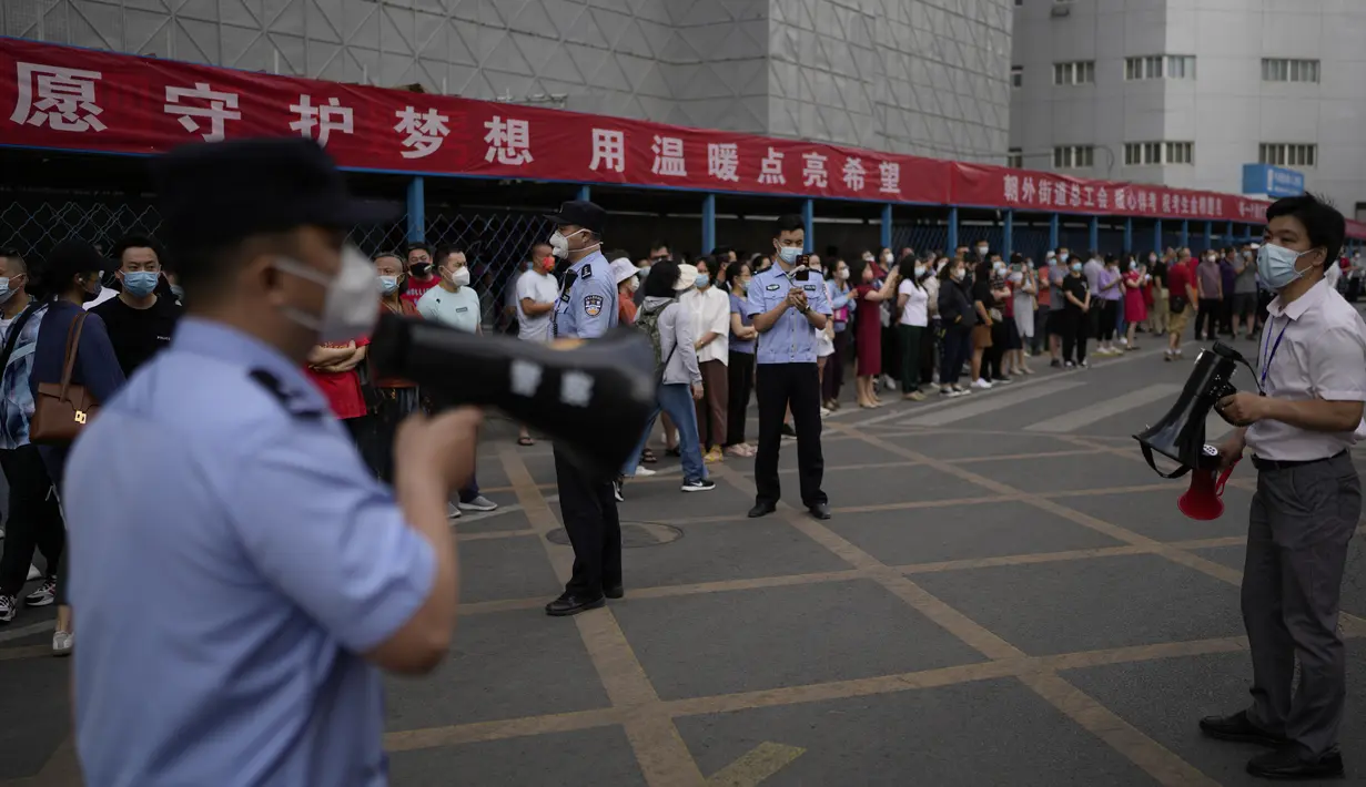 Seorang polisi dan petugas sekolah menggunakan pengeras suara untuk meminta kerabatnya mundur saat para siswa memasuki sekolah untuk hari pertama ujian masuk perguruan tinggi nasional China, di Beijing, Selasa (7/6/2022). Hasil dari ujian tersebut menjadi satu-satunya syarat diterima universitas di China. (AP Photo/Andy Wong)