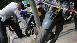 Petugas Dishub DKI menggembosi ban sepeda motor yang nekat parkir liar di trotoar sepanjang Jalan Kramat Raya, Senen, Jakarta, Jumat (22/9). Razia dilakukan untuk mengembalikan fungsi trotoar sebagai jalur pedestrian. (Liputan6.com/Faizal Fanani)