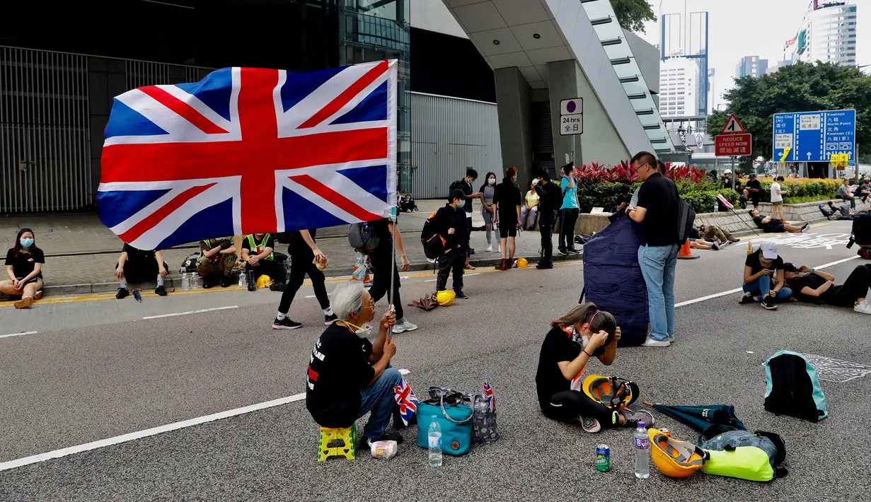 Seorang wanita memegang bendera Inggris ketika para demonstran beristirahat di sepanjang jalan utama dekat Gedung Dewan Legislatif saat menggelar protes terkait RUU Ekstradisi di Hong Kong, Senin (17/6/2019). (AP Photo/Vincent Yu)