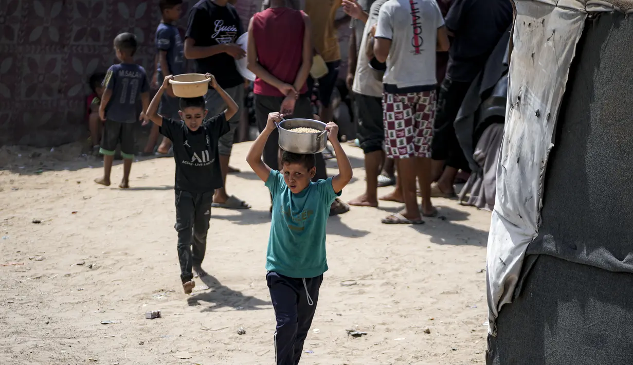 Anak-anak berjalan tanpa alas kaki di jalan tanah untuk membawa air dalam jeriken plastic, sementara yang lain menunggu di dapur umum dengan membawa wadah untuk membawa pulang makanan. (AP Photo/Abdel Kareem Hana)