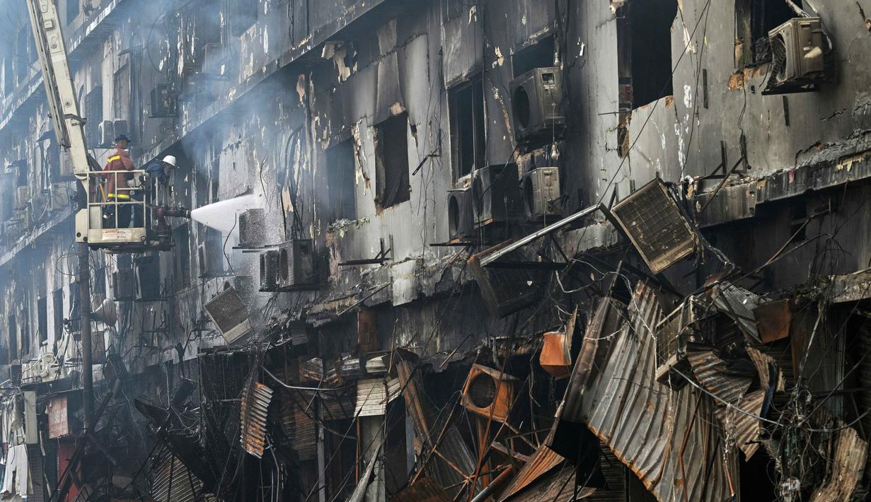 Sementara, puluhan orang lainnya masih dikabarkan hilang. Tampak dalam foto, petugas pemadam kebakaran melakukan operasi pendinginan pada bangunan yang terbakar setelah kebakaran besar di sebuah pusat perbelanjaan di Karachi pada Senin 19 Januari 2026. (Asif HASSAN/AFP)