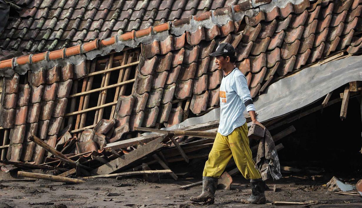 Di beberapa titik, jalan desa tertimbun material vulkanik hingga setinggi atap rumah. Tampak dalam foto, seorang pria menyelamatkan barang-barang dari sebuah rumah yang hancur akibat aliran piroklastik Gunung Semeru di Desa Supiturang, Lumajang, Jawa Timur, pada Jumat 21 November 2025. (Agus Harianto/AFP)