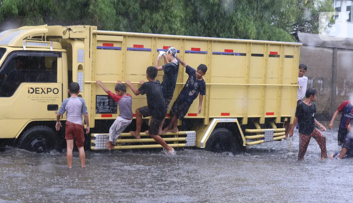 Sejumlah anak menaiki truk saat bermain banjir di jalan Bayangkara Pusdiklat, Kota Tangerang Selatan, Banten, Selasa (2/11/2021). Aksi anak anak tersebut dapat membahayakan keselamatan jiwa karena banyaknya kendaraan yang melintas menerjang banjir. (Liputan6.com/Angga Yuniar)