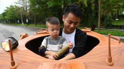 Truong Van Dao dan putranya menaiki tank kayu di daerah perumahan di provinsi Bac Ninh pada 28 Maret 2022. Seorang ayah di Vietnam telah menghabiskan ratusan jam dan menginvestasikan uangnya untuk mengubah mobil van tua menjadi tank kayu untuk putranya. (Nhac NGUYEN /AFP)
